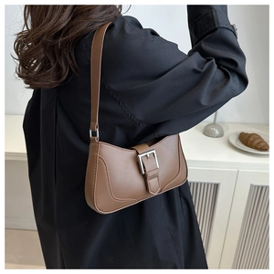 Brown leather crescent bag with silver buckle worn by a model in a minimalist setting