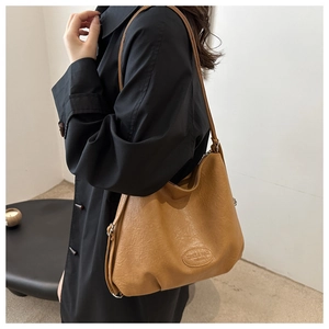 Close-up of brown textured leather shoulder bag featuring an embossed fashion logo detail