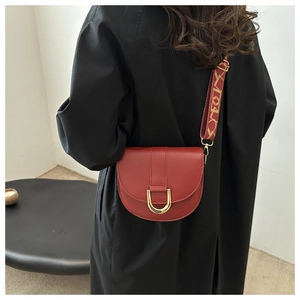 Detail of dark red saddle bag with gold U-shaped buckle and woven jacquard strap