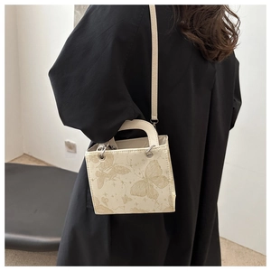 Detail view of cream square crossbody bag with gold butterfly prints and slim strap