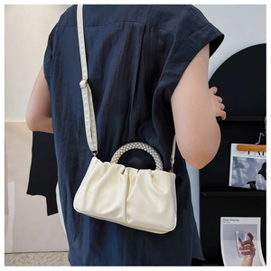Close-up of white pleated dumpling bag with pearl handle and leather strap on a model