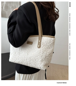 Detail of white plush tote bag with brown leather strap and brand label on shoulder