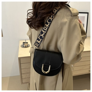 Detail of black leather saddle bag with golden horseshoe buckle and woven strap