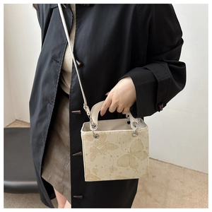 Detail of cream crossbody bag with gold butterfly print and metallic handle ring