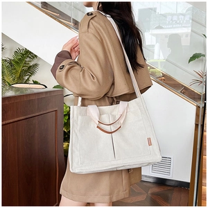 Detail of white corduroy tote bag featuring brown fashion label and adjustable strap