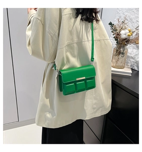 Minimalist green crossbody bag with textured squares shown on a model in a modern interior
