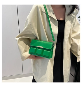 Detail of bright green crossbody bag with 3D square texture and gold metal bar accent