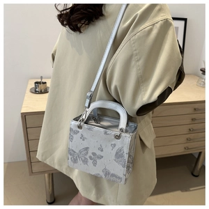 Detail of a silver square crossbody bag with glitter butterfly pattern and metal handle