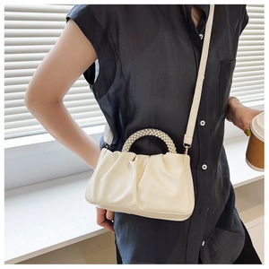Detail of cream pleated cloud bag featuring decorative pearl handle and leather strap