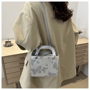 Detail of square bag with grey butterfly print shown on a model in a cozy indoor setting
