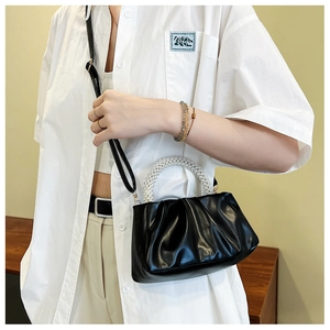 Detail of black pleated cloud bag with elegant large pearl handle and crossbody strap