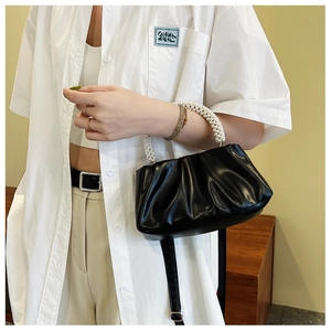 Detail of black pleated cloud bag with elegant white pearl handles and thin strap