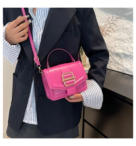 Sac bandoulière en cuir rose vif avec boucle dorée porté sur un blazer noir