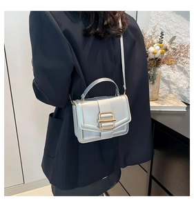 Détail d'un sac bandoulière argenté avec boucle dorée porté à l'épaule par un mannequin