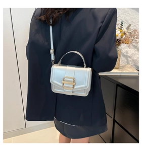 Sac carré chic en similicuir argenté avec fermoir doré porté par un mannequin en décor