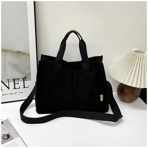 Detail of black corduroy tote bag showing fashion tag, outer pocket and adjustable strap