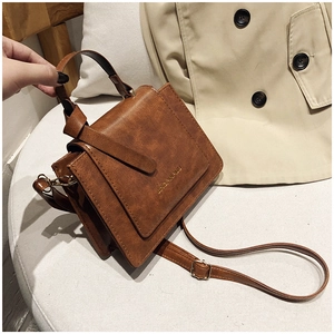 Détail d'un sac à main marron vintage sur canapé blanc avec un trench classique