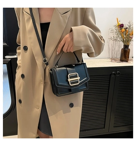 Détail d'un sac bandoulière en cuir noir avec boucle dorée sur un trench-coat beige