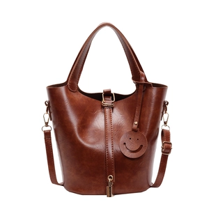 Sac seau marron classique avec poignée et breloque sourire sur un fond blanc neutre