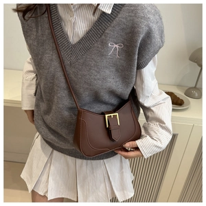 Détail du sac bandoulière demi-lune en cuir marron avec boucle dorée sur un mannequin