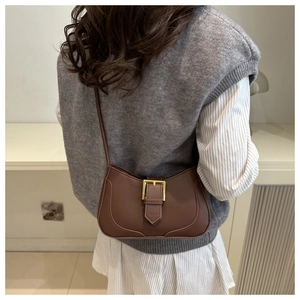 Détail du sac croissant en cuir marron foncé avec boucle dorée sur l'épaule d'un mannequin
