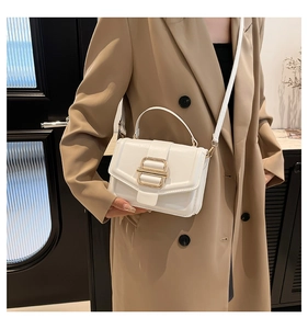Détail du sac à bandoulière en cuir blanc avec boucle dorée sur un trench-coat beige