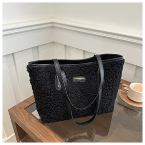Detail of black sherpa tote bag featuring a gold metal logo plate and premium leather handles