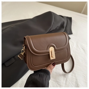 Close-up of brown leather crossbody bag with gold buckle and fine stitching details