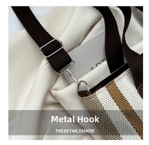 Detail of silver metal hook and brown woven strap on striped canvas tote bag