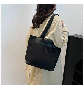 Detail of black corduroy tote bag showing leather reinforced bottom on beige trench coat