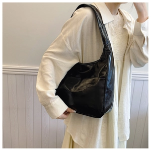 Detailed side view of high-gloss black oil wax leather tote bag worn by a model