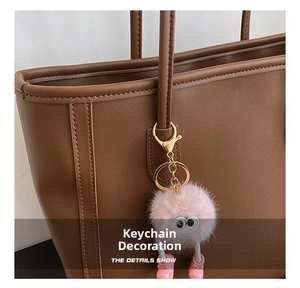 Pink furry monster charm with large eyes and boots hanging on a leather tote bag