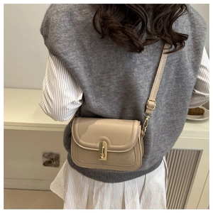 Detail of beige minimalist crossbody bag with gold twist lock on a model's back