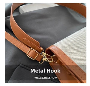 Detail of gold metal hook and buckle on brown leather and beige canvas shoulder bag