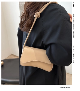 Detail of beige underarm bag with curved bottom and knot strap on a black coat