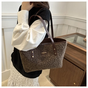 Detail of plush brown tote bag featuring leather brand tag and metal rivet accents
