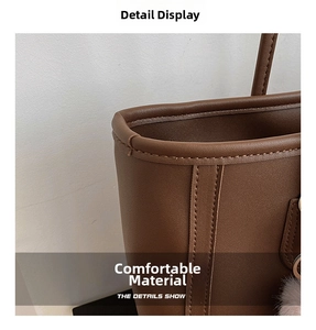 Detail view of brown leather handbag featuring precision stitching and a pink pompom charm
