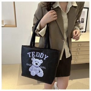 Quilted black puffer tote bag detail featuring large teddy bear print and soft texture