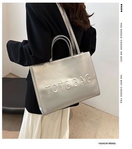 Detail of silver metallic tote bag featuring 3D embossed TOTE BAG lettering and dual straps