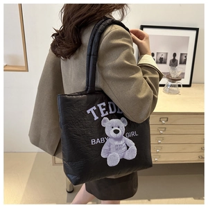 Detail of black quilted tote bag featuring purple teddy bear print and text worn by model
