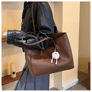 Detail of a large dark brown matte leather tote bag with a pink monster plush charm