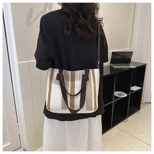 Detail of striped canvas tote bag showing dark brown woven handles and adjustable shoulder strap