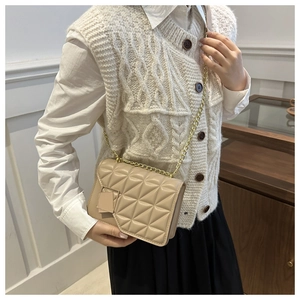 Sac bandoulière beige matelassé avec chaîne dorée porté par un mannequin en gilet chic