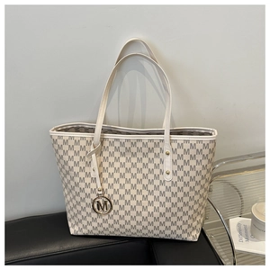 Detailed close-up of large tote bag with M-letter pattern and gold metal pendant charms