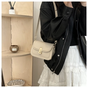 Detail view of a cream crossbody bag with gold metal clasp on a leather jacket