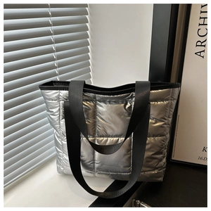 Detail of silver metallic quilted tote bag with black straps and puffy texture design