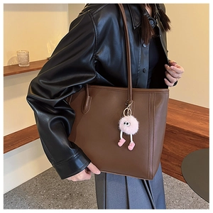 Detailed view of brown leather tote bag with a pink plush doll pendant and fine stitching