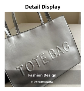 Close-up of embossed TOTE BAG lettering on silver metallic faux leather tote bag
