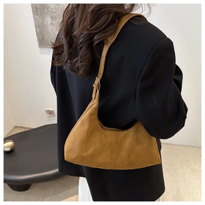 Sac hobo en daim marron porté sur un blazer noir pour un style minimaliste et chic