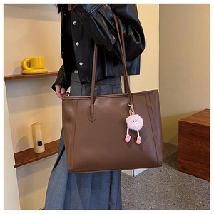 Close-up of a brown leather tote bag featuring a cute pink plush monster bag charm